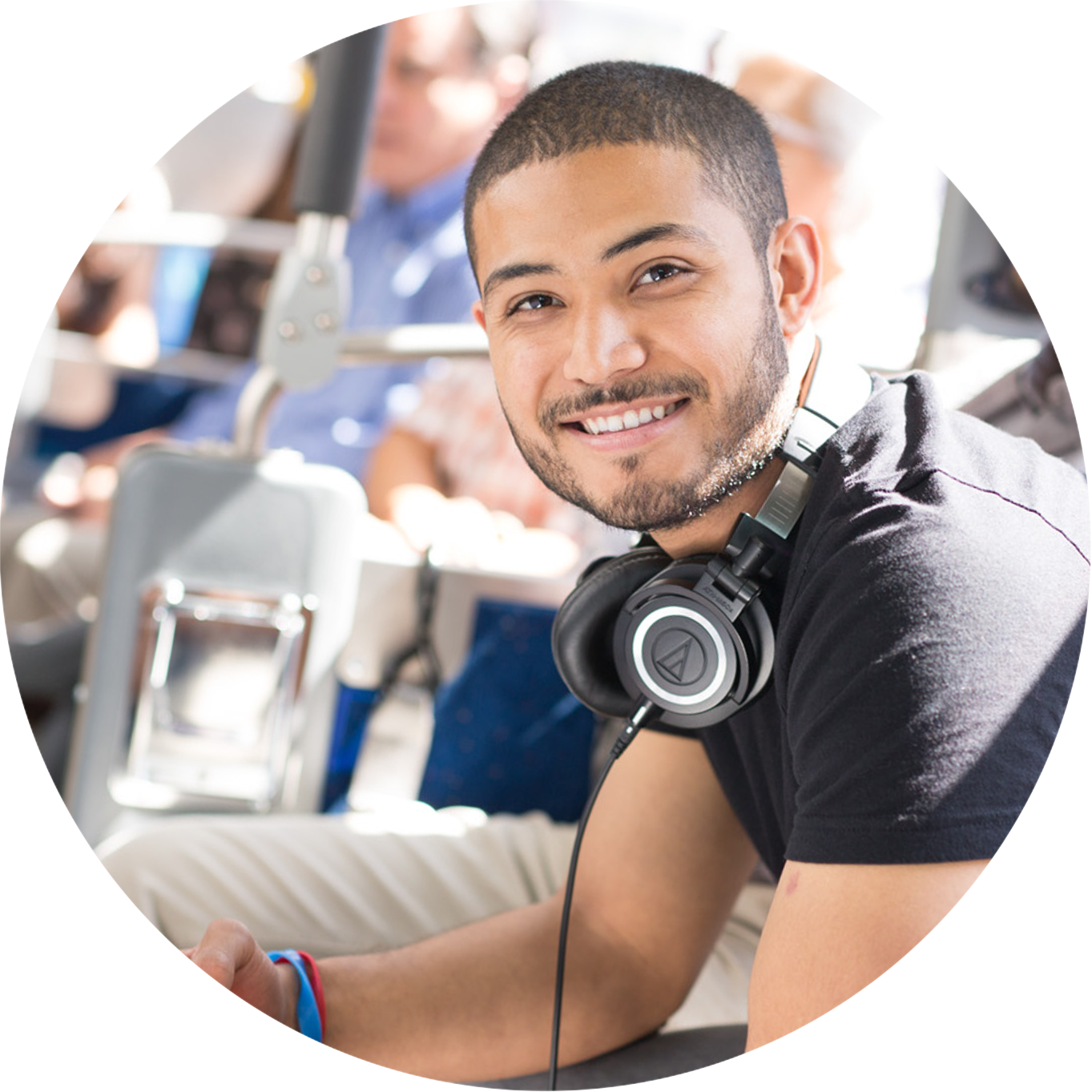 a smiling man riding riding a bus with a pair of headphones hanging on his neck